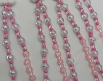 May include: Several beaded lanyards featuring a white cat charm with a pink bow. The lanyards have pink and clear beads, with the name "MARIE" spelled out in pink letter beads.