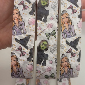 May include: Three white keychains with silver rings. Each keychain features a different character from the movie 'Wicked' with a white background and pink, green, and gold accents.