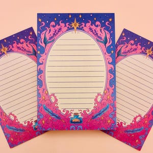 May include: Three notepads with a fantasy theme. Each notepad has a pink and blue decorative border with an oval space for writing. The borders feature stars, flames, and a potion bottle. The background is a light peach colour.
