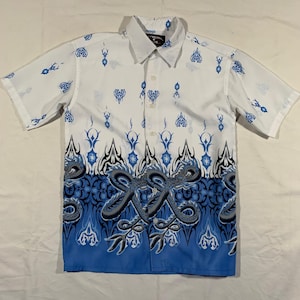 Puede incluir: Camisa blanca de manga corta con botones y estampado de dragón azul y negro. La camisa tiene un patrón azul y blanco en la mitad inferior.
