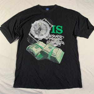 Puede incluir: Camiseta negra con un gráfico verde "IS", un reloj con incrustaciones de diamantes y fajos de dinero. El texto "TIME MONEY" también es visible en la camiseta.