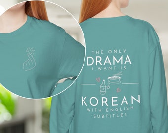 Puede incluir: Camiseta de manga larga verde mar con el texto "THE ONLY DRAMA I WANT IS KOREAN WITH ENGLISH SUBTITLES" en blanco. La camiseta presenta un gráfico de gesto de la mano en la manga izquierda y un gráfico de comida coreana en la espalda.