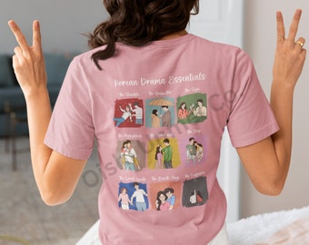 May include: A pink t-shirt with a graphic print of nine scenes from popular Korean dramas. The text "Korean Drama Essentials" is printed at the top of the graphic. The scenes include "The Stumble", "The Umbrella", "The Sign", "The Piggyback", "The Hand Pull", "The Vow", "The Wrist Grab", "The Back Hug", and "The Confession".