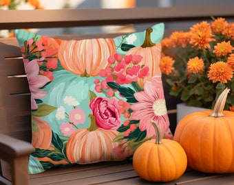May include: A teal and pink throw pillow with a floral pattern featuring pumpkins and flowers. The pillow is on a wooden bench with two orange pumpkins in the foreground.