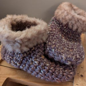 Puede incluir: Un par de zapatillas de crochet de color morado y blanco con ribete de piel sintética.