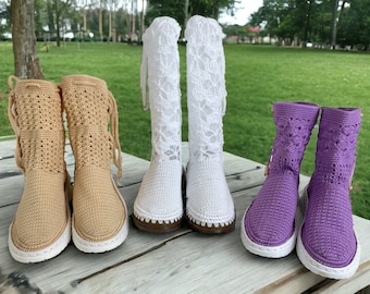 May include: Four pairs of crochet boots in tan, white, and purple. The tan boots have an open weave design. The white boots are tall with a lace pattern. The purple boots have a floral pattern. All boots have white soles.