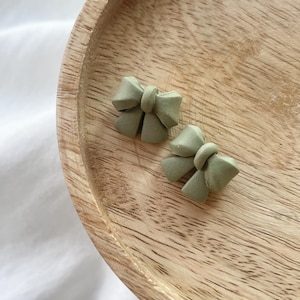 May include: Two small green bow-shaped earrings on a wooden surface.