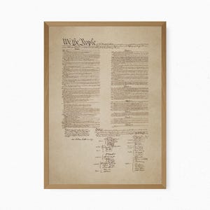 May include: A framed print of the United States Constitution on aged, parchment-style paper. The document features the prominent heading We the People in black ink, followed by multiple columns of text and a list of signatures at the bottom.