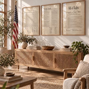 May include: A long wooden media console with three cane-webbed doors sits below three framed prints of the Declaration of Independence, the Constitution, and the Bill of Rights. The console is light brown with a natural finish and vertical handles.