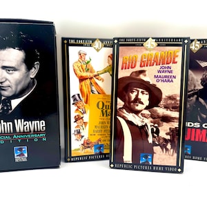 Peut inclure: Trois cassettes VHS présentant des films classiques de John Wayne. Les cassettes sont noires avec des lettres dorées et présentent des images de John Wayne dans chaque film. Les titres sont "John Wayne Special Anniversary Edition", "Rio Grande" et "Les Sables d'Iwo Jima".