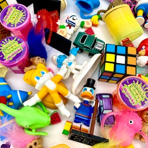 May include: A collection of assorted toys including a yellow Tails figure, a Donald Duck figure, a Rubik's cube, several Bedwina mini noise putty containers, a green toy car, a red Knuckles figure, troll dolls, and various small plastic figurines.