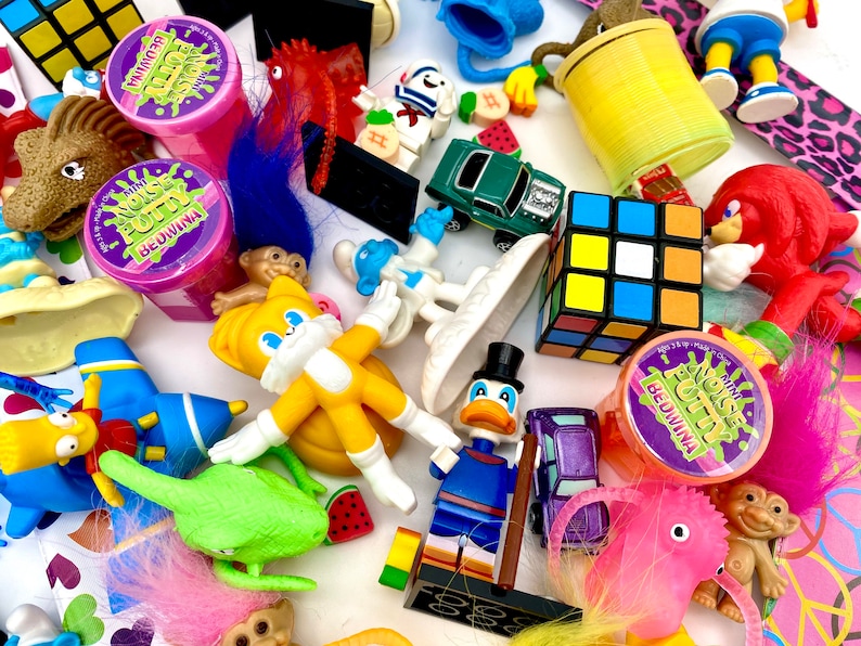 May include: A collection of assorted toys including a yellow Tails figure, a Donald Duck figure, a Rubik's cube, several Bedwina mini noise putty containers, a green toy car, a red Knuckles figure, troll dolls, and various small plastic figurines.
