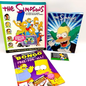 May include: A collection of The Simpsons merchandise, including a book titled "The Simpsons: A Complete Guide to Our Favorite Family", a DVD box set, and a comic book. The book features the Simpsons family on the cover.