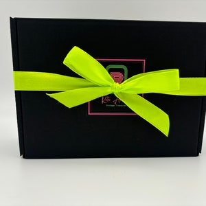 May include: A rectangular black cardboard box wrapped with a bright neon yellow satin ribbon tied in a bow. Centered on the front is a square logo featuring a stylised letter R in green and pink, with the text Retro A Vintage Treasures below.