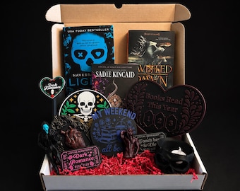 May include: A gift box containing three books titled Light, Twisted Dawn, and a Sadie Kincaid novel. Included are a heart-shaped tracker labeled Books Read This Year, a skull sticker, a Dark Romance ticket, a heart-shaped sign, and a black skull candle holder.