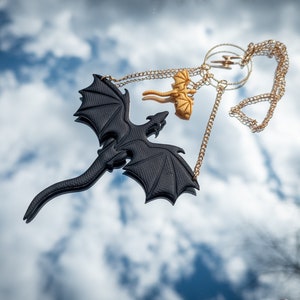 May include: A black dragon pendant necklace with a gold chain. The dragon is flying with its wings spread wide. There is a smaller gold dragon pendant on the chain as well.