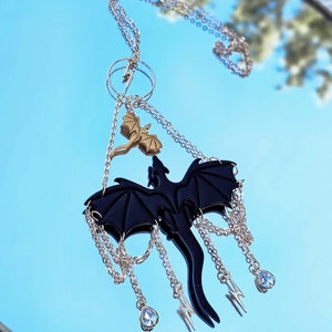 May include: A silver chain necklace with a black dragon pendant and a smaller gold dragon charm. The pendant has multiple silver chains with crystal accents hanging from it.