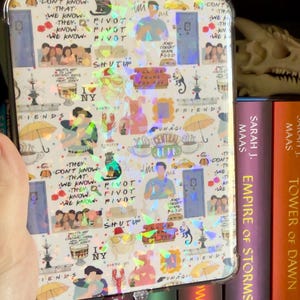 May include: A clear phone case with a holographic design featuring images and phrases from the TV show Friends. The case includes images of the characters, quotes like "Pivot," and iconic elements like the Central Perk logo.