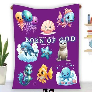 May include: Purple blanket featuring cartoon sea creatures like jellyfish, fish, and a dolphin. The text "THIS CHILD IS BORN OF GOD" is displayed in white. A decorative item for a nursery or child's room.