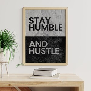 May include: A framed motivational poster with a black and white grunge background. The text on the poster reads "Stay Humble and Hustle".