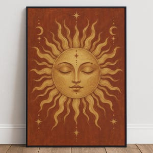 May include: A rectangular wall art print featuring a central golden sun with a human face, closed eyes, and swirling cheek details. The sun has wavy rays and is set against a deep terracotta background with small golden stars and crescent moons.