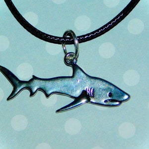 May include: A silver shark pendant necklace with a black cord. The shark is detailed with a fin and gills.