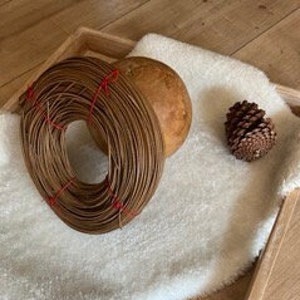 Könnte beinhalten: Ein Holztablett mit einer weißen Kunstfell-Auskleidung. Auf dem Tablett befinden sich drei natürliche Gegenstände: ein großer brauner geflochtener Kranz, eine kleinere braune Holzschale und eine kleine braune Kiefernzapfen.