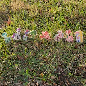 Könnte beinhalten: Eine Sammlung bunter Comic-Pony-Aufkleber auf grünem Gras. Die Aufkleber zeigen verschiedene Pony-Charaktere mit verschiedenen Gesichtsausdrücken und Posen.