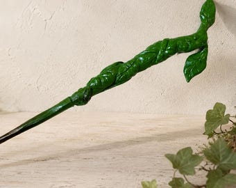 Op de afbeelding: Een groene toverstaf met een gestructureerd, wijnrankachtig handvat dat om de schacht is gewikkeld, uitlopend in een puntig uiteinde aan de ene kant en een decoratief, bladvormig uitsteeksel aan de andere kant, met een glanzende afwerking.