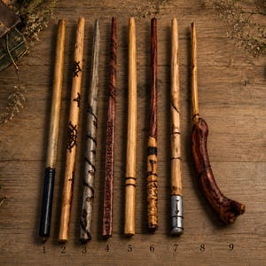 Puede incluir: Nueve varitas de madera dispuestas verticalmente, con diversos acabados y tallas. Las varitas varían de color tostado claro a marrón oscuro, algunas con detalles metálicos, patrones en espiral y un mango curvo, grueso y de color marrón rojizo.