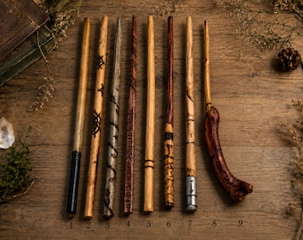 May include: Nine wooden wands arranged vertically, featuring various finishes and carvings. The wands range from light tan to dark brown, with some showing metallic accents, spiral patterns, and one curved, thick, dark reddish-brown handle.