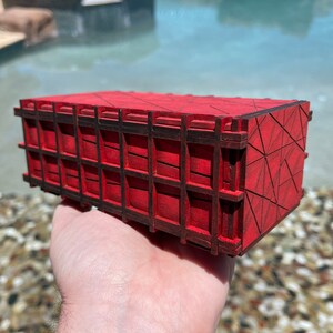 May include: A small, red wooden box with a geometric pattern on the top and sides. The box is made of multiple pieces of wood that are joined together to create a lattice-like design.