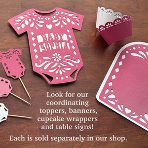 May include: A set of pink and white paper die-cut decorations including a large onesie cutout with the text BABY SOPHIA, three small onesie cupcake toppers on wooden picks, a scalloped cupcake wrapper, and a large arched sign with decorative borders.