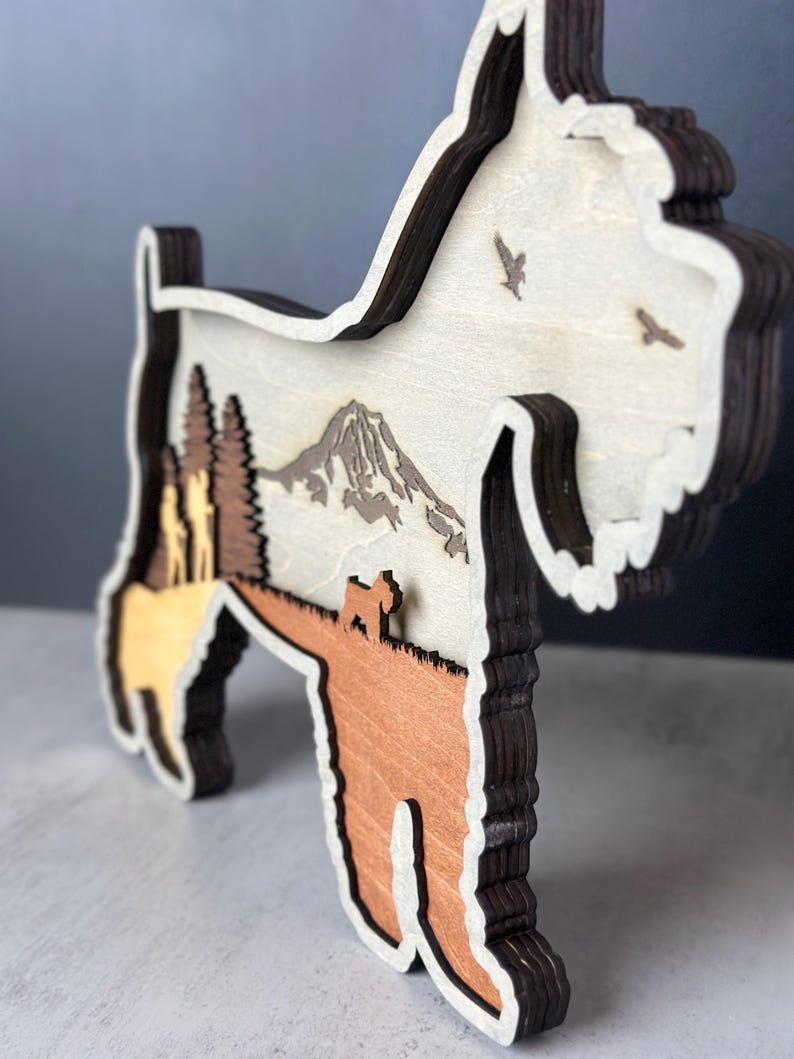 Puede incluir: Silueta de madera en capas de un perro Schnauzer con una escena de monta&ntilde;a y bosque. El perro es marr&oacute;n, beige y en tonos de madera natural, con un contorno marr&oacute;n oscuro. Dos p&aacute;jaros vuelan en el cielo. Es un objeto decorativo.