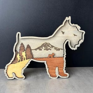 Puede incluir: Escultura de schnauzer en miniatura de madera con un dise&ntilde;o en capas. La escultura presenta una escena de monta&ntilde;a y una silueta de perro. El texto "DOG LOVER GIFT" es visible. La escultura mide unos 18 cm de largo.