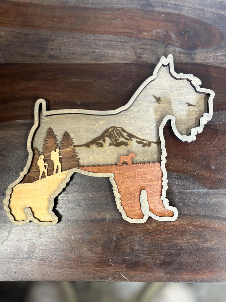 Puede incluir: Recorte de madera con forma de perro y dise&ntilde;o en capas. El interior presenta una escena de monta&ntilde;a con excursionistas y &aacute;rboles. Las patas del perro son de color marr&oacute;n anaranjado c&aacute;lido, mientras que el cuerpo es de tono madera natural. Dos p&aacute;jaros vuelan en el cielo.
