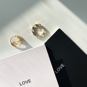 Może przedstawiać: Dwa złote pierścionki na białym tle z napisem "LOVE" na biało-czarnym notesie.