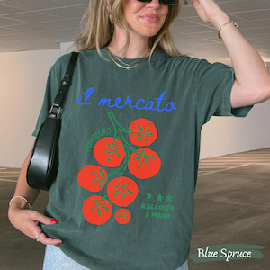 May include: Blue spruce t-shirt with a tomato graphic. The design includes the words "il mercato" in blue script, a cluster of red tomatoes, and the words "RACCOLTO A MANO".