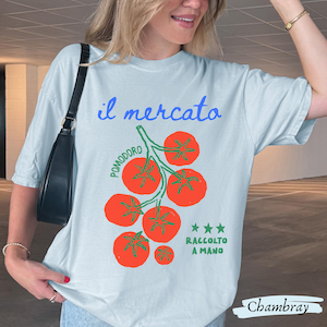 May include: Light blue t-shirt with the Italian text "il mercato" and a graphic of red tomatoes on a green vine. The text "Pomodoro" and "Raccolto a Mano" are also present. The word "Chambray" is written at the bottom.