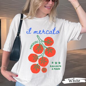 May include: White t-shirt with a tomato graphic. The design includes the Italian words "il mercato" and "pomodoro," along with "raccolto a mano." The graphic features red tomatoes and green stems. The word "White" is printed at the bottom.