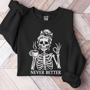 May include: Black sweatshirt featuring a white skeleton design. The skeleton is holding a coffee cup and giving an "okay" sign. The words "NEVER BETTER" are printed below the image.