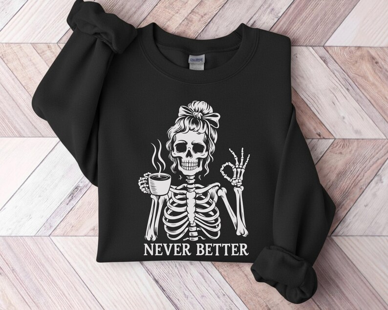 May include: Black sweatshirt featuring a white skeleton design. The skeleton is holding a coffee cup and giving an "okay" sign. The words "NEVER BETTER" are printed below the image.