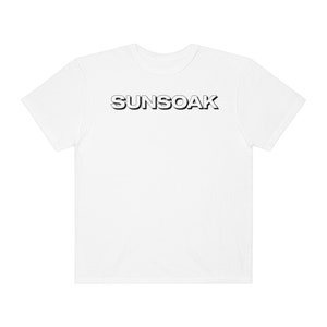 May include: White t-shirt with the word "SUNSOAK" printed in black on the front.