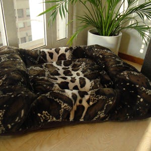 May include: A patterned pet bed in shades of brown and white. The bed has a rectangular shape with raised sides and a central cushion. The fabric has a soft, textured appearance, suitable for a dog or cat.