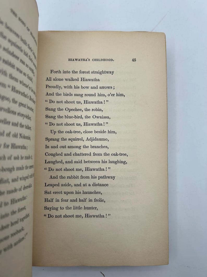 May include: Open book with text from "Hiawatha's Childhood" on a cream-colored page. The text includes lines like "Do not shoot us, Hiawatha!" and is set in a classic serif font. The page number 45 is visible.