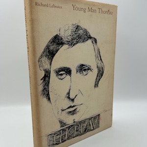 May include: A vintage book titled "Young Man Thoreau" by Richard Lebeaux. The cover features a black and white illustration of a man's face and the name "THOREAU" in a stylized font. The book has a worn, beige cover.
