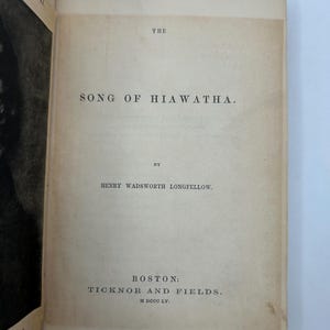 May include: Open book with the title "The Song of Hiawatha" by Henry Wadsworth Longfellow. Published by Ticknor and Fields in Boston. The page is aged with a light tan color.