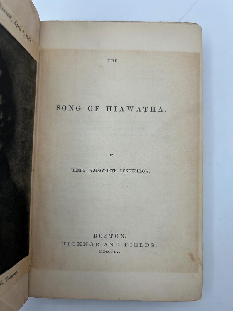 May include: Open book with the title "The Song of Hiawatha" by Henry Wadsworth Longfellow. Published by Ticknor and Fields in Boston. The page is aged with a light tan color.
