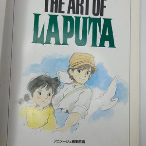 May include: A book cover featuring the title "THE ART OF LAPUTA" in black and green lettering. Below the title is an illustration of two children with doves. The book is a collection of art from the animated film.