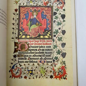 May include: An illuminated manuscript page featuring a detailed illustration of a seated figure in a red throne, surrounded by ornate floral and foliate borders. The page includes Latin text and decorative elements in red, blue, and gold.